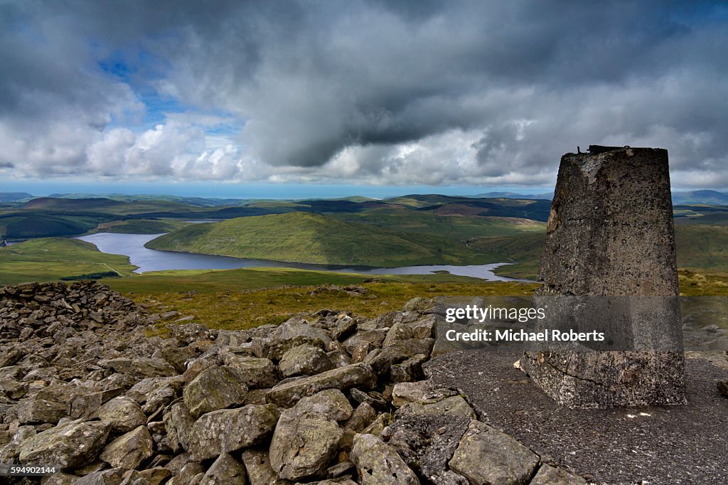 The trig point on the summit of Plynlimon, or Pen Pumlumon Fawr, overlooking Nant-y-Moch reservoir in the Cambrian mountains, Wales