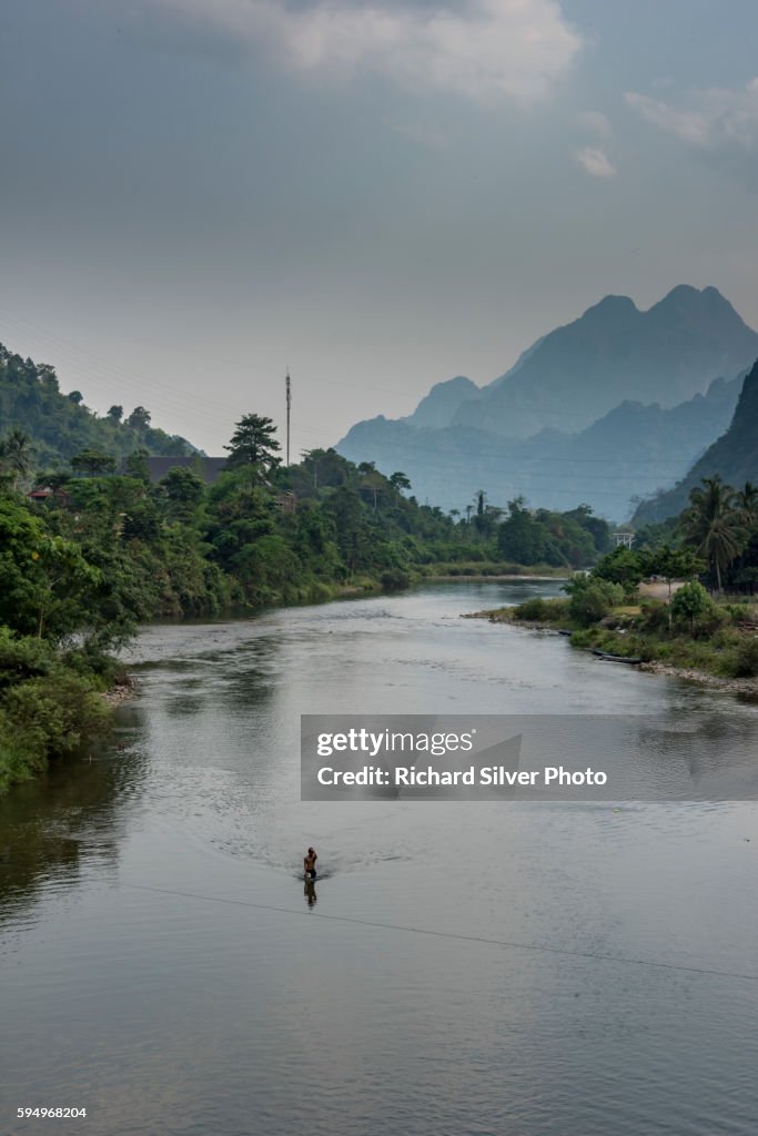 Man on a boat on a river with mountains in Vang Vieng, Laos