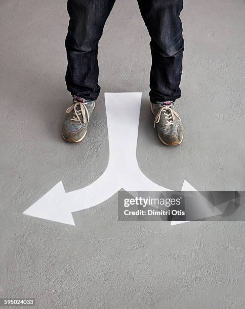 mans feet standing in front of arrow floor marking - bivio foto e immagini stock