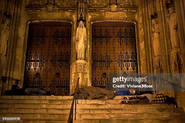 Homeless men asleep on the front steps of St. Thomas church on 5th Avenue, sheltered by the giant wooden doors, and the statue of Jesus Christ and...