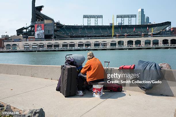 Homeless man stares across McCovey Cove towards ATT Park, the baseball stadium of the San Francisco Giants, in the China Basin neighborhood of San...