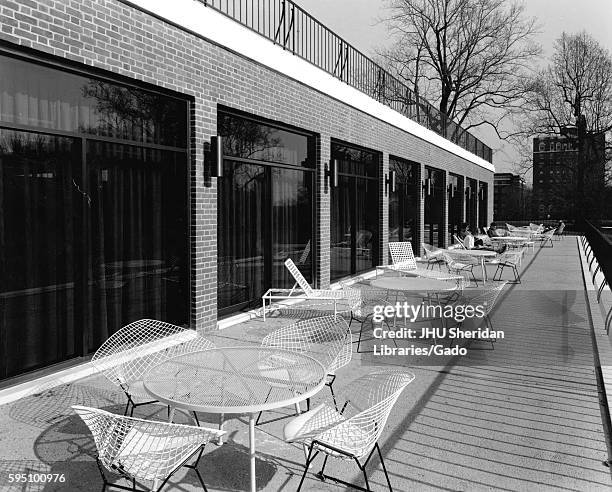 Outside of the Milton S Eisenhower Library at Johns Hopkins University, a terrace with tables, chairs, and lounge chairs borders the perimeter of M...