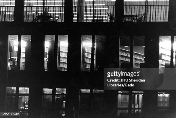At nighttime, the levels inside the Milton S Eisenhower Library light up the windows, showing stacks of books and the silhouettes of students working...