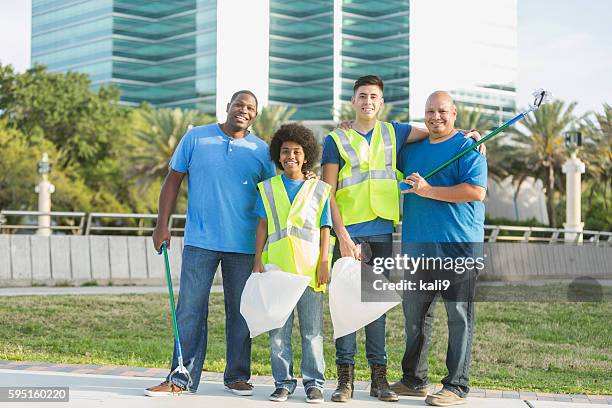 multi-ethnic fathers and son helping the community - vuilniszak stockfoto's en -beelden