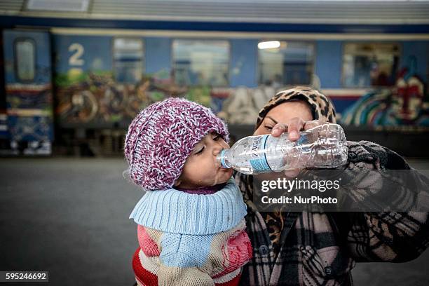 Syrian girl drinking in carried by her mother on March 17, 2016 in Thessaloniki rail station. Between Athens and the border with Macedonia, many...