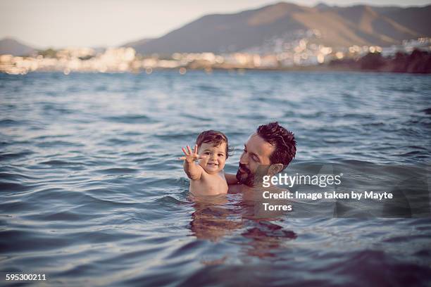 baby girl with dad having a swim at the beach - baby schwimmen stock-fotos und bilder