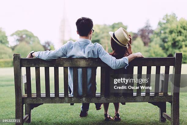 young couple sitting on bench in park - public park bench stock pictures, royalty-free photos & images
