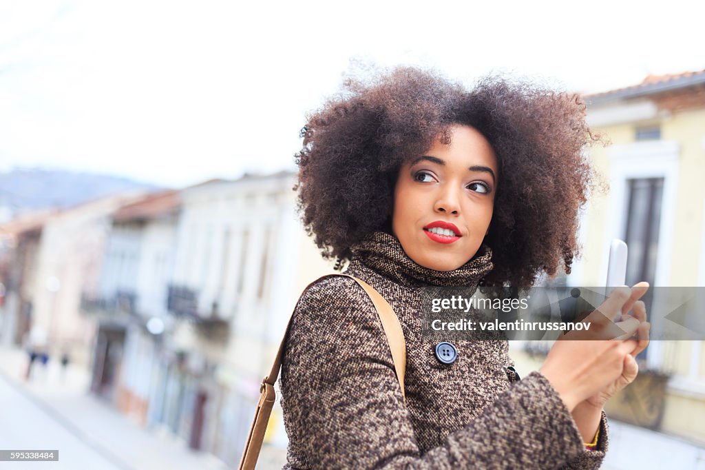 Beautiful young woman using smart phone on street