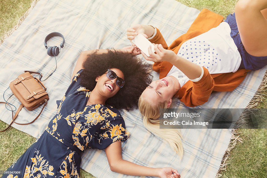 Friends taking selfie relaxing on blanket in grass