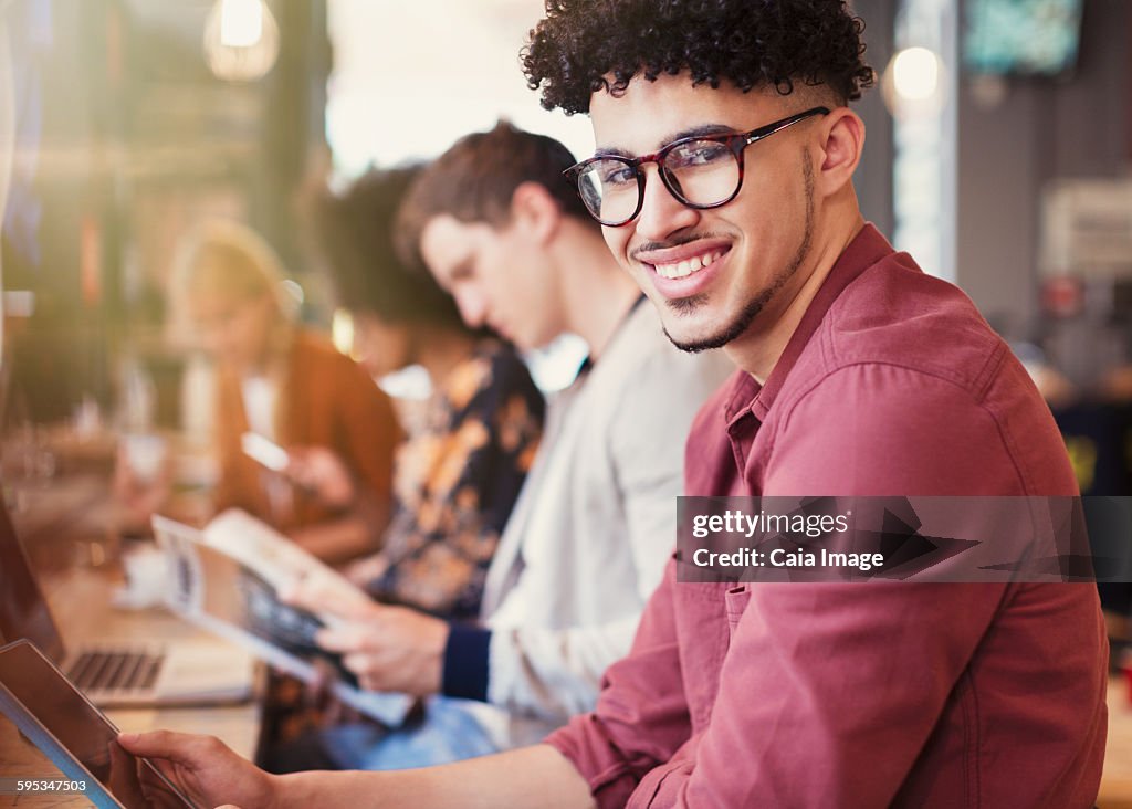 Portrait smiling man with curly black hair using digital tablet in cafe