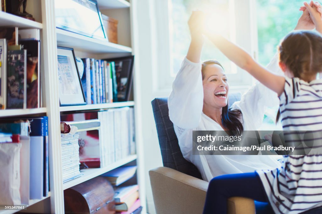 Enthusiastic mother and daughter holding hands overhead