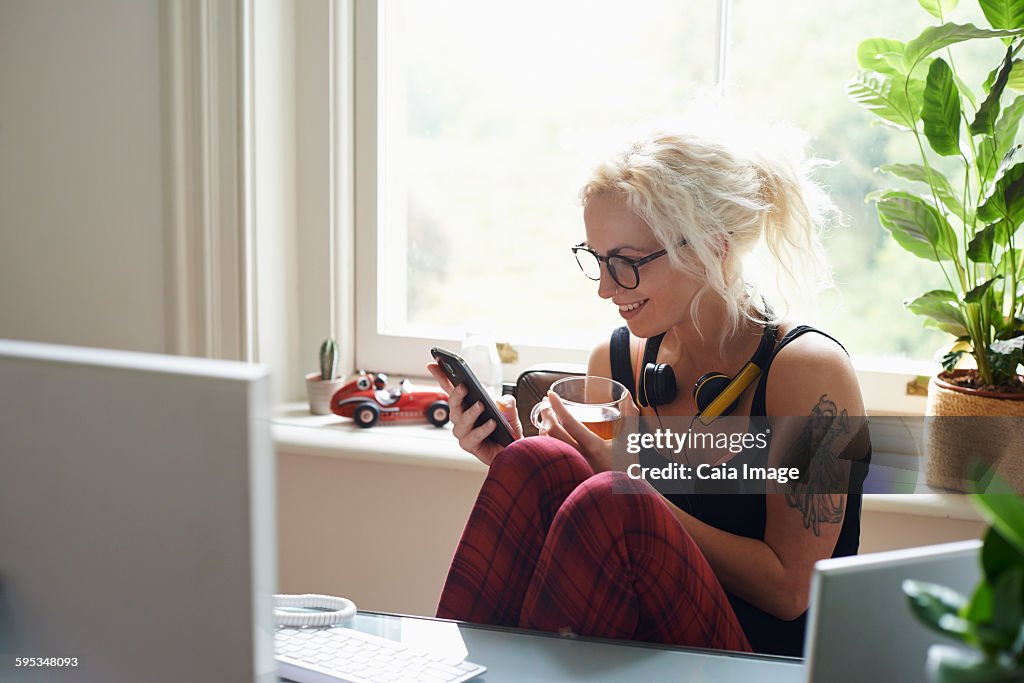 Young woman with headphones and tattoo texting in home office