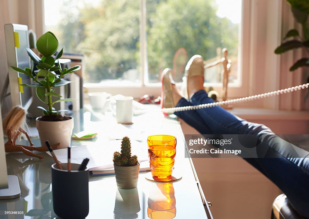 Woman talking on telephone with feet up on desk in sunny home office