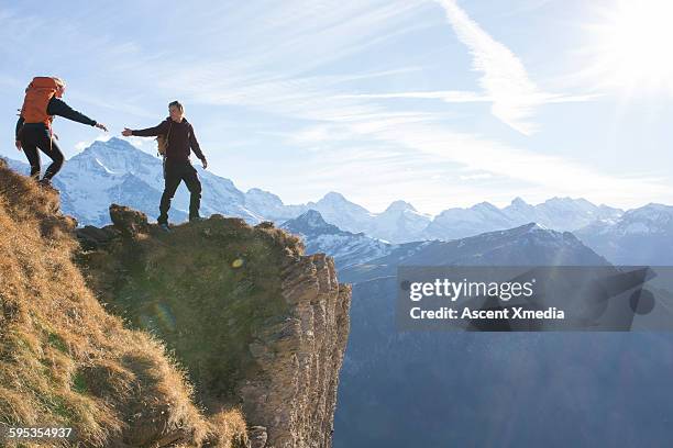 hiker offers companion a helping hand, above mtns - trust fotografías e imágenes de stock