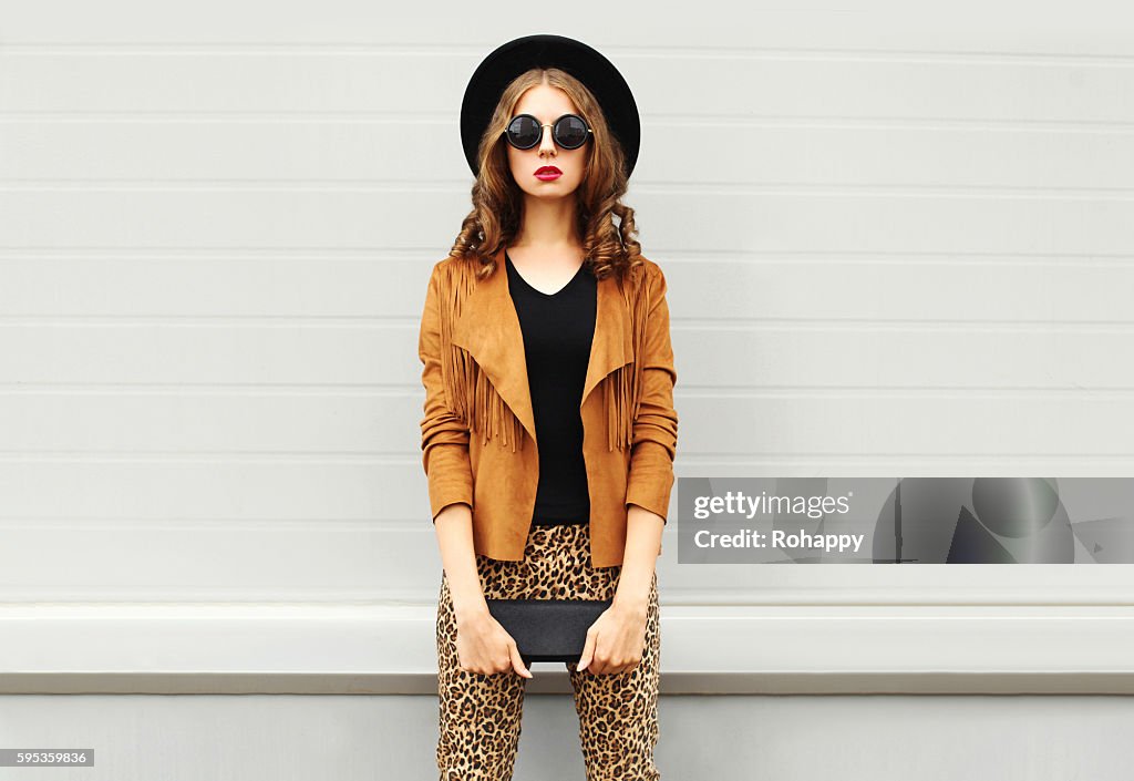 Fashion woman wearing elegant hat, jacket handbag clutch over background