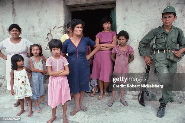 At the doorway of a building, a group of women and children look at a Salvadoran Army soldier , Verapaz, El Salvador, April 1983. The Army had just...