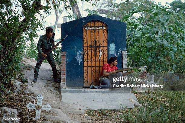Salvadoran Army soldier and a member of a civil defense militia take cover in a neighborhood cemetery during combat , San Salvador, El Salvador,...