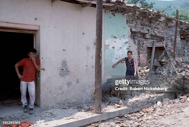 Two people stand outside a heavily-damaged home, San Vicente department, El Salvador, May 1983. The building was damaged in a battle between the...