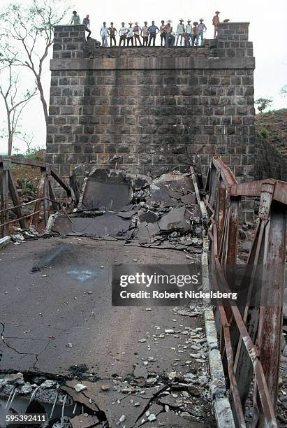 View, from below, of people as they stand on the remains of a collapsed bridge, central El Salvador, circa June 1983. The bridge was allegedly...