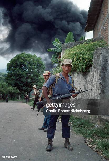View of Ejercito Revolucionario del Pueblo guerillas as they stand on the street, San Miguel, El Salvador, September 1983. The smoke in the...