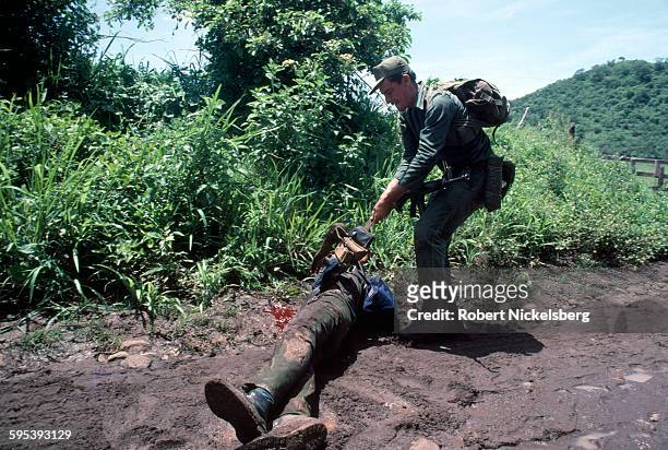 Salvadoran Army soldier, of the Atlacatl Battalion, removes the weapons belt of a dead Ejercito Revolucionario del Pueblo guerrilla, San Miguel...
