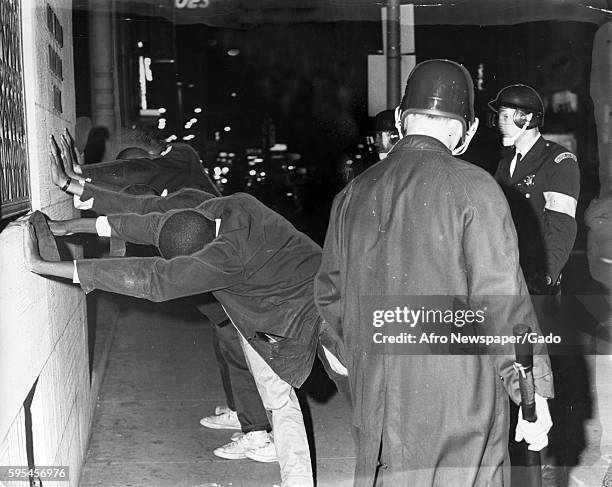 At the intersection of Bradford and Lanvale streets in Baltimore, Maryland, Caucasian riot policemen holding billy clubs and helmets check suspected...