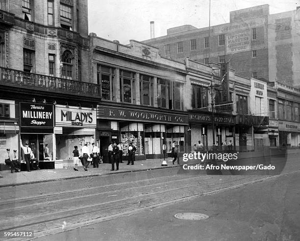 In front of an FW Woolworth Co store on North Howard Street in Baltimore, Maryland, African-American citizens walk down the sidewalk amid a heavy...