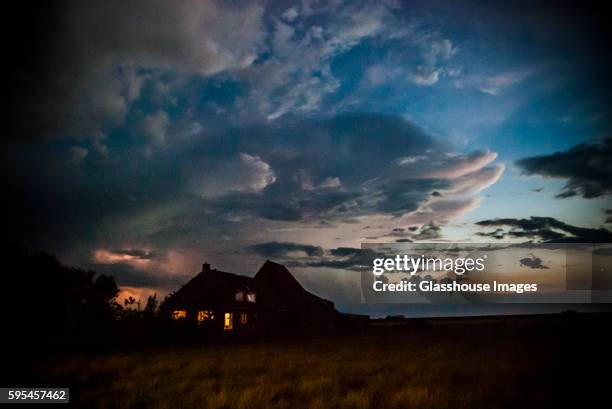 dark farm house under turbulent sky during electrical storm - bauernhaus stock-fotos und bilder