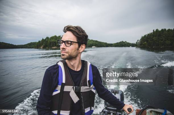 young adult man wearing life jacket driving motor boat on lake - steering boat stock pictures, royalty-free photos & images