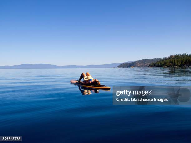 woman laying down on paddleboard on lake - lake tahoe stock pictures, royalty-free photos & images