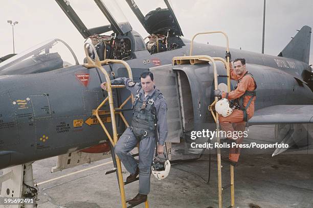 Two Royal Navy pilots stand on access ladders beside a Royal Navy Fleet Air Arm McDonnell Douglas F-4K Phantom II at an airbase near the McDonnell...