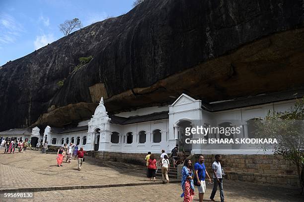 Foreign tourists walk past the entrance to a natural cave at the Rock Temple, also known as the Rangiri Dambulla Rajamaha Viharaya, in Dambulla, some...