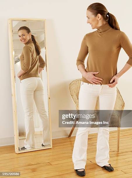 mid-adult trying on jeans - woman-looking-into-mirror-full-body stock pictures, royalty-free photos & images