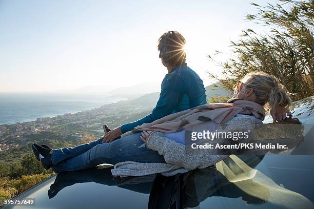 couple relax on car hood, look out to hills, sea - sitting on top of car stock pictures, royalty-free photos & images