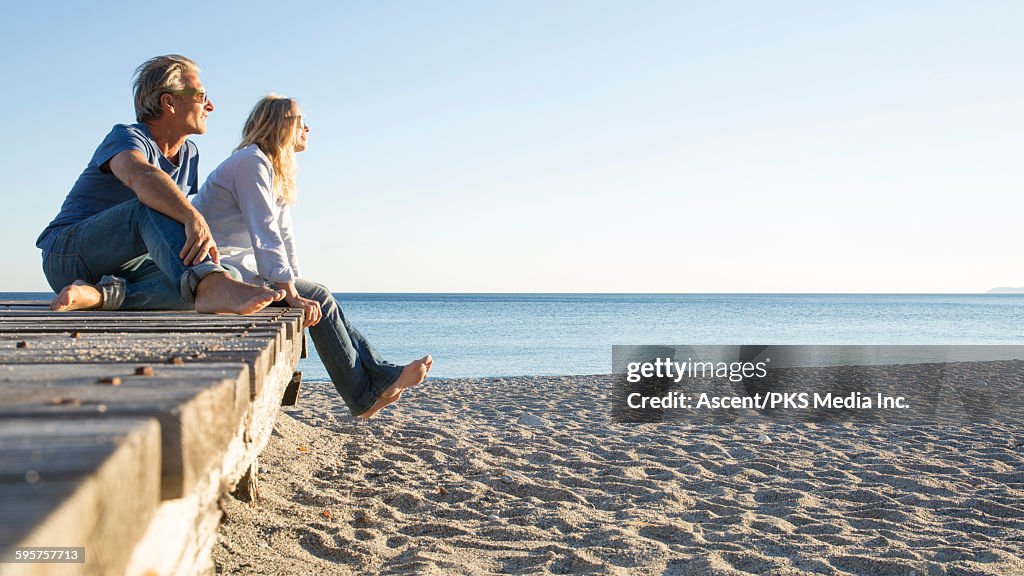 Couple relax on beach boardwalk, look off to sea
