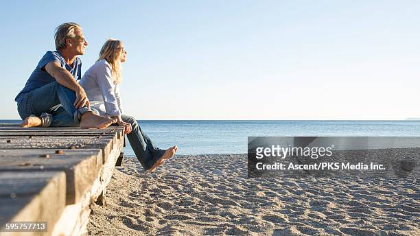 couple relax on beach boardwalk, look off to sea - paso entablado fotografías e imágenes de stock