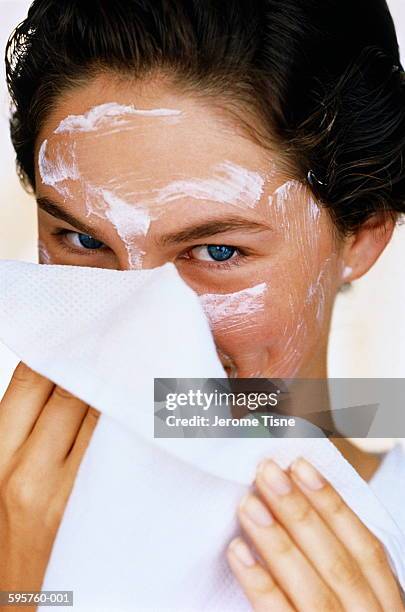 young woman wiping white face cream off with towel, close-up - máscara facial fotografías e imágenes de stock