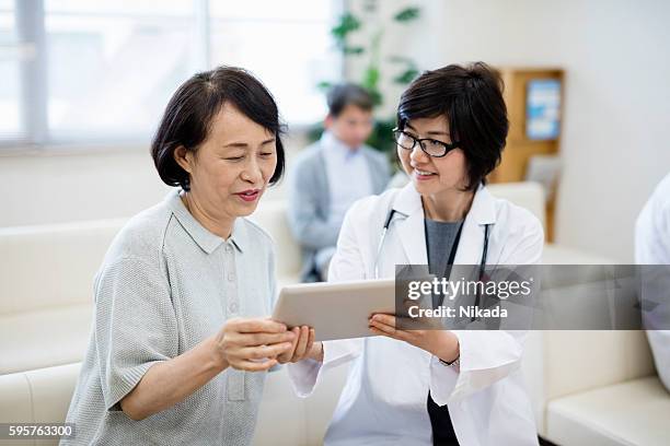 female doctor showing digital tablet to patient in hospital - japanese old woman stock pictures, royalty-free photos & images