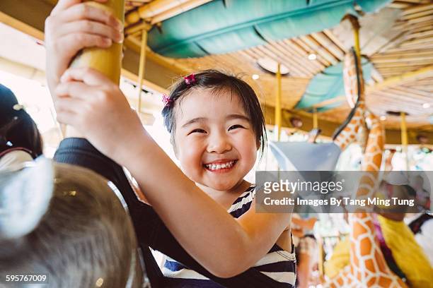 lovely little girl riding on a carousel joyfully - parque de diversiones fotografías e imágenes de stock