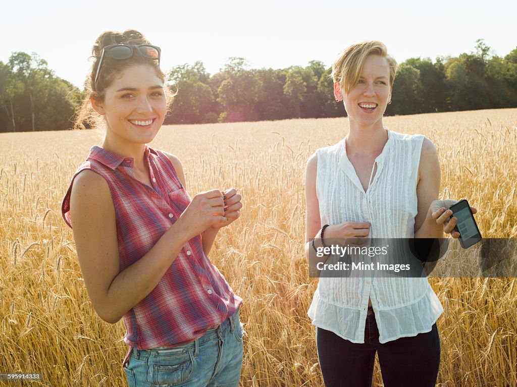 Two smiling young women standing in a cornfield, one holding a smart phone. 