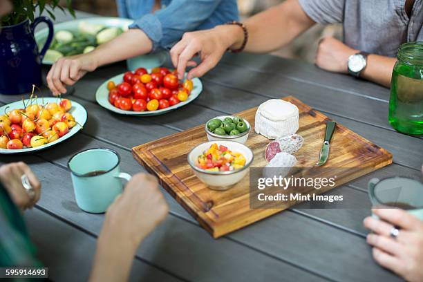 a group of people gathered around a table with plates of fresh fruits and vegetables, and a round cheese and salami on a chopping board.  - round four bildbanksfoton och bilder