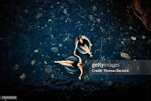 friends holding hands floating in inner tubes - opblaasband stockfoto's en -beelden