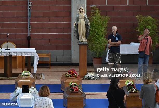 People stand next to the coffins of earthquake victims, in a gymnasium arranged in a chapel of rest on August 26 in Ascoli Piceno, two day after a...