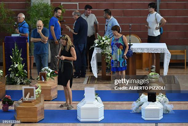 People stand next to the coffins of earthquake victims, in a gymnasium arranged in a chapel of rest on August 26 in Ascoli Piceno, two day after a...