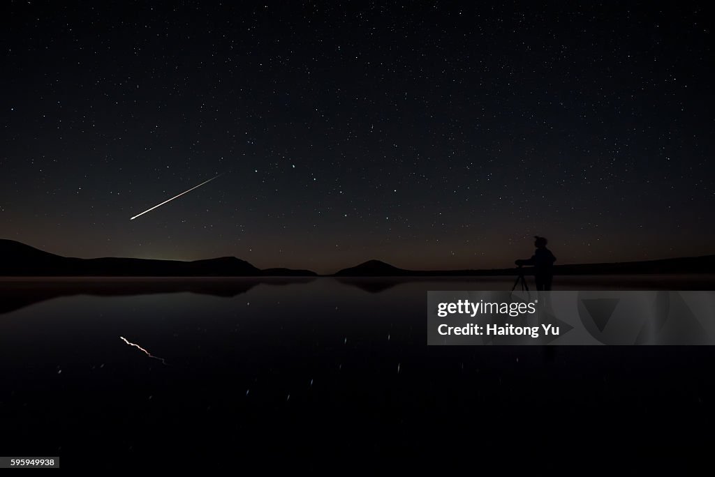 A bright meteoroid flying past as a man setting up his camera inside a lake