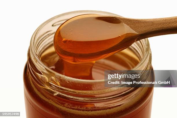 manuka honey running into jar from wooden spoon - manuka honey stock pictures, royalty-free photos & images