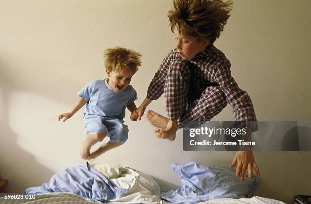 two young boys (4-9) bouncing on bed - children jumping bed stock-fotos und bilder