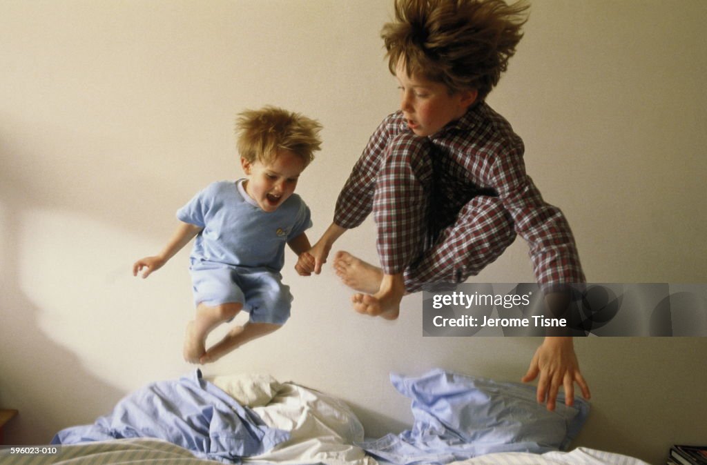 Two young boys (4-9) bouncing on bed