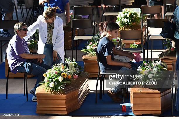 Relatives of earthquake victims sit next to coffins, in a gymnasium arranged in a chapel of rest on August 27 in Ascoli Piceno, three days after a...