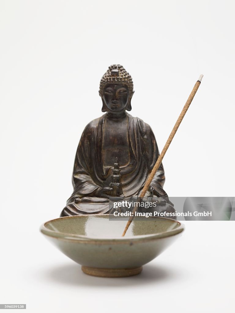 Incense stick in ceramic dish in front of Buddha figure